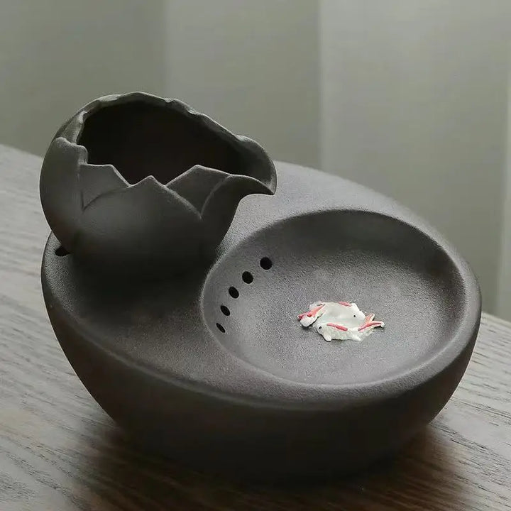 Cendrier en argile noir en forme d'œuf avec un petit pot fissuré, design moderne.